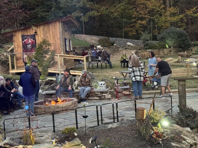Firepit gathering at Mountain Harbour, cozy outdoor entertainment in the mountains, autumn foliage, rustic wooden cabin setting.