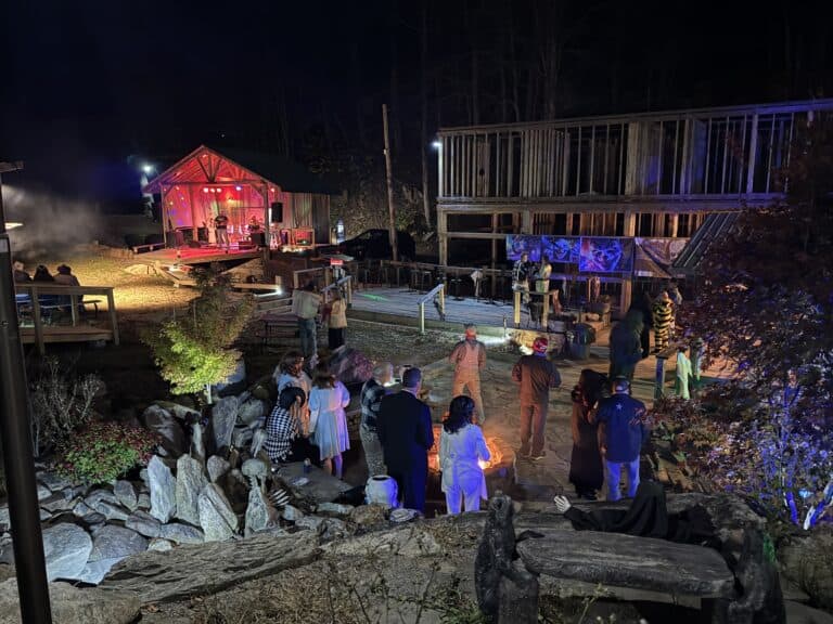 Mountain Harbour outdoor evening music event with people enjoying a concert in a scenic mountain setting, illuminated by colorful lights.